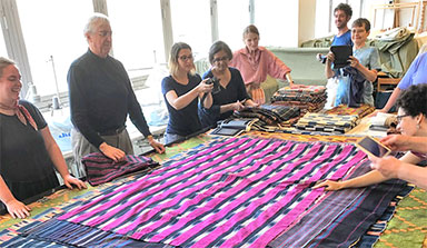 A group stands around a table with ikat textiles on it