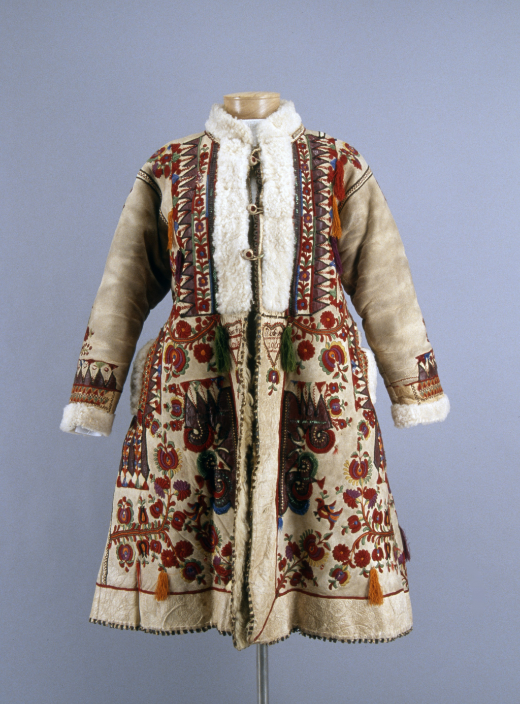 An embroidered coat that is closed at the front with three large buttons. There is furr along the collar, opening, and cuffs. The coat is on a mannequin.